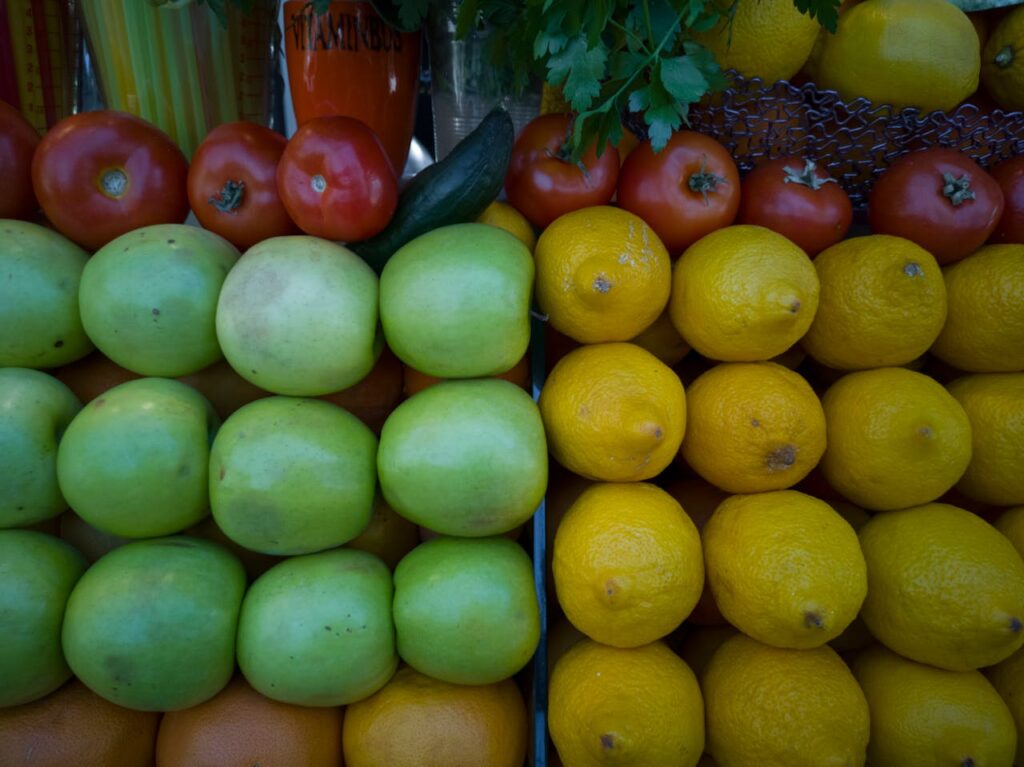 Colorful array of tomatoes, apples, and lemons on a market stall, showcasing freshness.