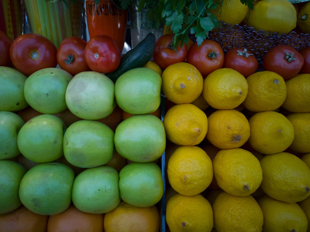 Colorful array of tomatoes, apples, and lemons on a market stall, showcasing freshness.